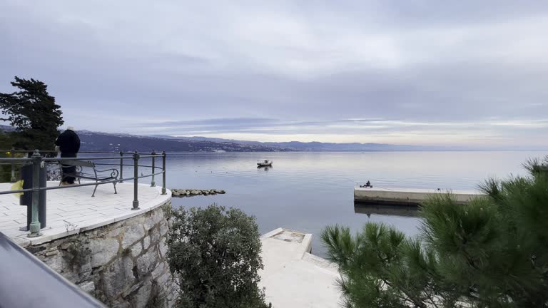Fisherman on peer Boat parked on Sea shore with town in distance extra wide, Opatija, Croatia