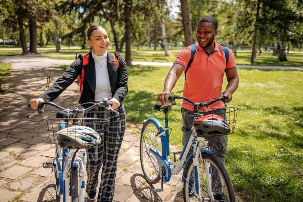 istock Two colleagues going to work walking through public park and pushing bikes 2150289938