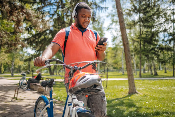 istock Young black man walking in public park holding mobile phone while pushing bike 2150290020