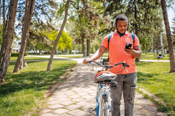 istock Young black man walking in public park holding mobile phone while pushing bike 2150290030