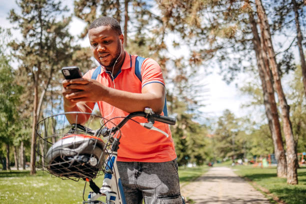 istock Young black man walking in public park holding mobile phone while pushing bike 2150290040