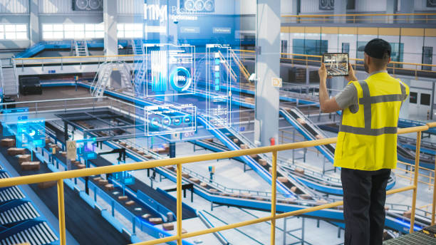 istock Male in a High Visibility Vest Using Tablet with Augmented Reality App. Worker Monitoring Efficiency in a Logistics Center with Automated Belt Conveyors for Sorting Retail Orders. VFX Visualization 2150292380