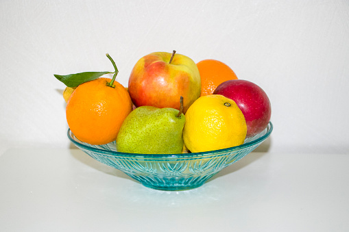 Fruits on a plate. Apples, pear, oranges, lemon. Whole fruits in a glass bowl on a white background.