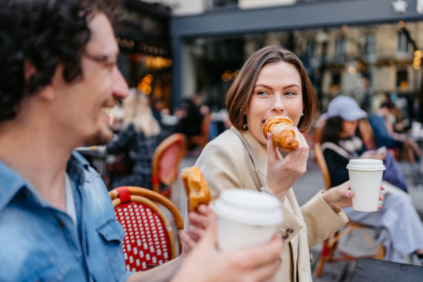 junges paar trinkt kaffee und isst croissants in einem straßencafé in paris - woman eating croissant stock-fotos und bilder