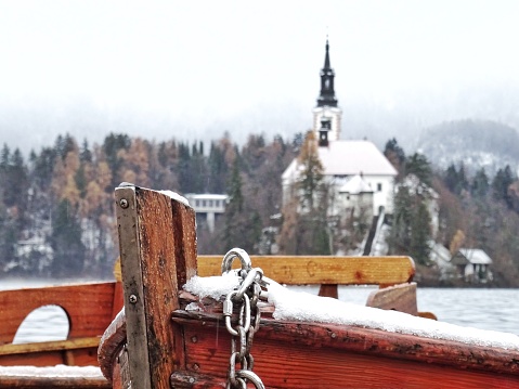 A picture of a boat at Lake Bled, Slovenia in winter, with the Pilgrimage Church of the Assumption of Mary in the background