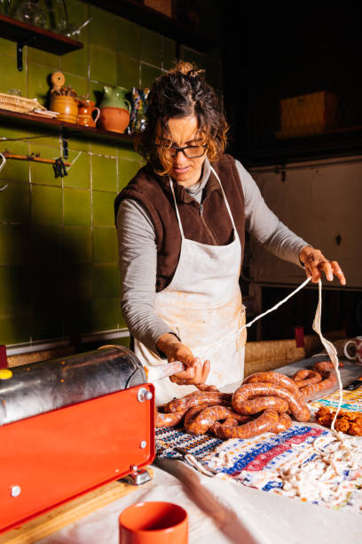 Woman preparing homemade sausages in kitchen using stuffer machine