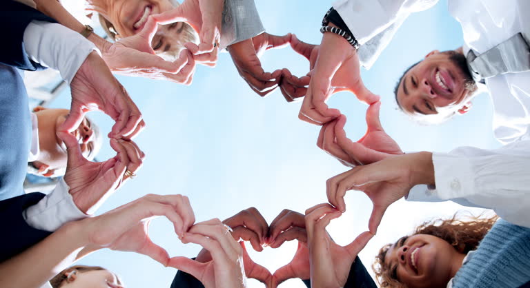 Love, wellness or business people with heart hands, care gesture or sky in community collaboration. Low angle, health or group of employees with teamwork support, symbol or thank you sign outdoors