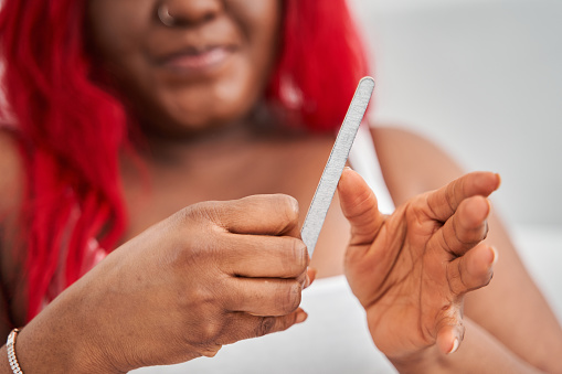 Cropped view of the oversize red haired woman doing manicure with nail file while spending time at home. Stock photo