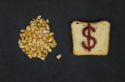 Cornbread with dollar sign. Corn grain. Black background. Costs, price increase.