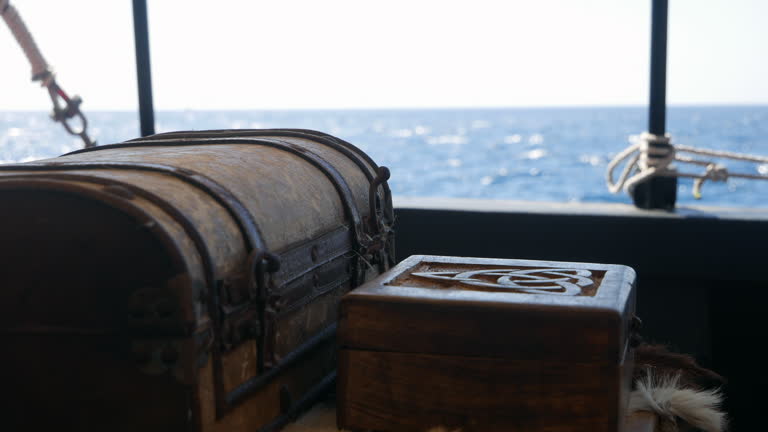 Vintage treasure chest and ornate wooden box on ship, shimmering sea in the sunlight. Nautical voyage, pirate chest, seafaring ambiance