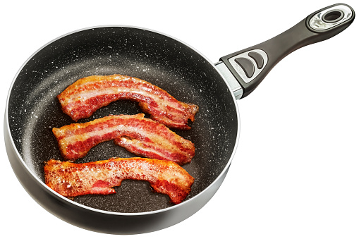 Traditional fried crispy crunchy gourmet bacon rashers in a large new modern heavy duty black Wok frying pan, with non-slip ceramic double coated inner surface, isolated on white background, high angle view.