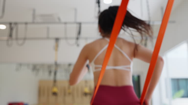 A woman is running on a treadmill with a red and orange strap around her waist