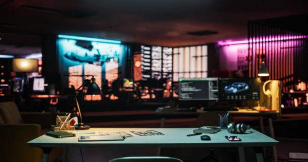Wide Shot of Desk with Smartphone, Laptop Computer and Notebook, Placed in an Empty Creative Office at Night. Modern Open Space Lit By Neon Lights for Game Development and Visual Media Production