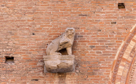 Architectural detail featuring a stone lion sculpture on a brick wall in Bologna. The sculpture sits on a base, adding a decorative aspect to the building exterior