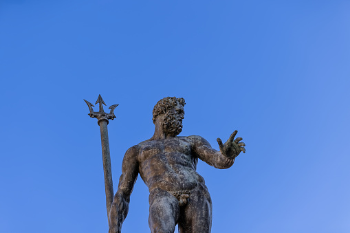 The bronze Neptune reaches towards the heavens, trident in hand, at Bologna Fountain of Neptune, set against a serene blue backdrop