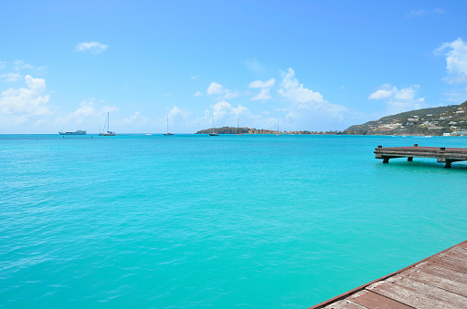 Beautiful torquoise water in a caribbean bay with a wooden pier, blue skies and clouds