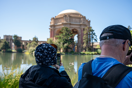 Mature woman and man photographing Rotunda of Palace of Fine Arts of San Francisco and its pond and fountain during springtime day