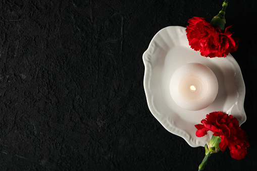Candle and flowers on black background, space for text