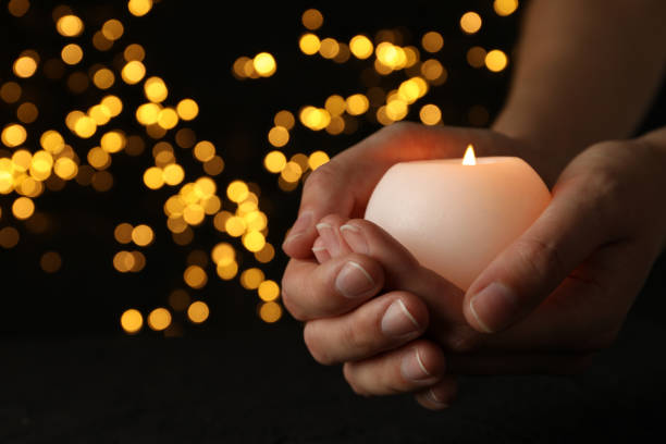 istock Mourning candles in hands, on a dark background. 2150310873