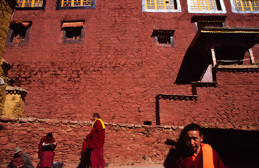 Group of buddhist monks in traditional attire walking by the vibrant walls of a Ganden monastery, Tibet