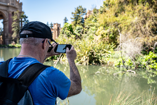 Mature man photographing a pond in San Francisco during springtime day