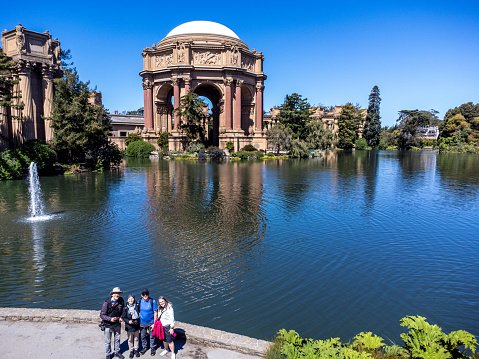 Aerial view of Palace of Fine Arts in San Francisco during springtime day with pond in foreground and four tourists looking at camera.