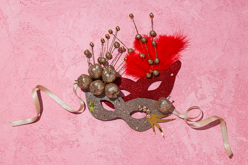 Carnival masks and feathers on pink background, top view