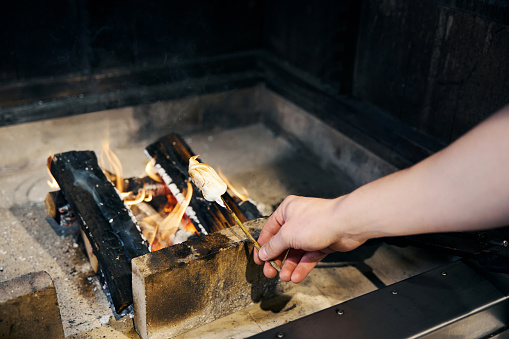 Partial male chef hand frying marshmallow on tree branch in burning fire place in restaurant. Concept of tasty healthy eating