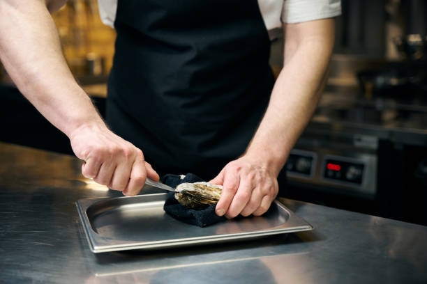 istock Cropped chef opening oyster with knife on iron tray for cooking dish at table 2150321451