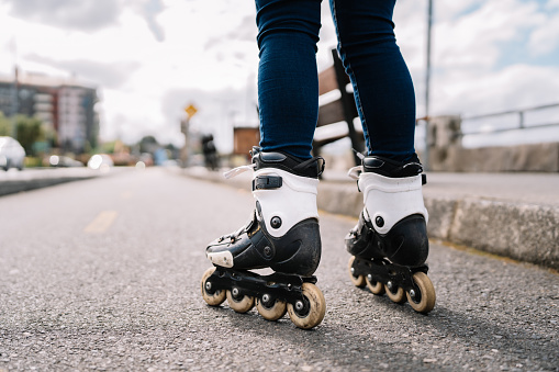 A woman is riding a roller skate on a city street. The skateboard is on a road with cars in the background