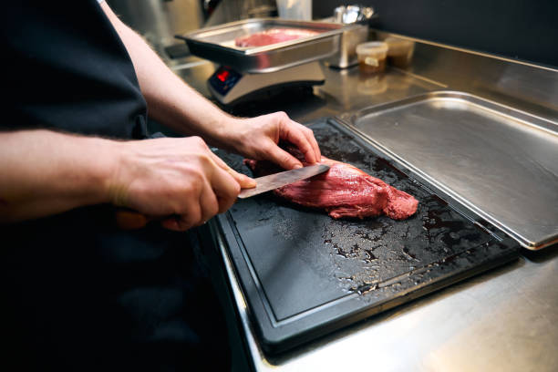 istock Partial male chef cutting meat fillet with knife on chopping board at table 2150323767