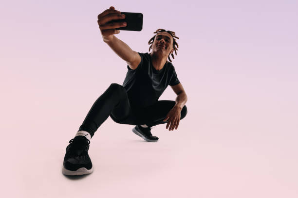 Fit Gen Z man takes a selfie in a studio with pink background.