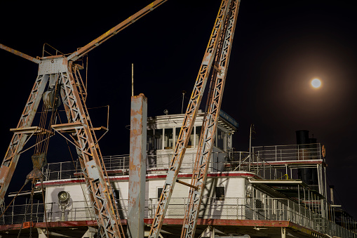 Brownville, NE, USA - April 22, 2024: Vintage sidewheeler dredge, Captain Meriwether Lewis,  displayed in a dry dock on a shore of the Missouri River, night view with full moon.