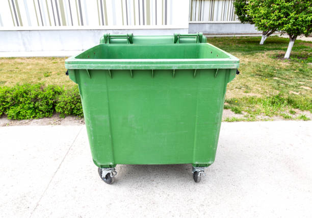 Opened big green plastic garbage container with wheels at the sunny city street