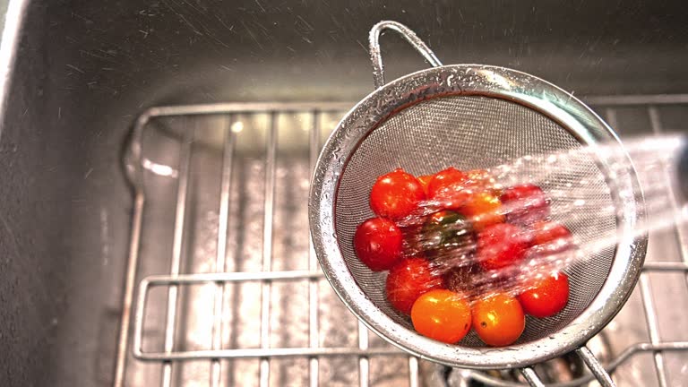 Washing little tomatoes inside strainer with riser hose in sink slow motion video