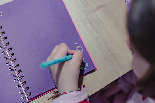 Left handed girl drawing on a purple notebook