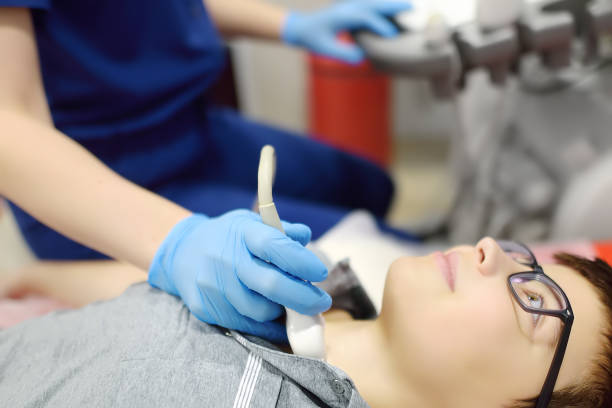istock Doctor making ultrasound of the thyroid gland for boy using scanner machine. Female doc runs ultrasound sensor over patient neck for scanning of the thyroid gland and lymph nodes. 2150331410