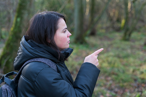Young woman pointing to the left in the forest. Focus on the left.