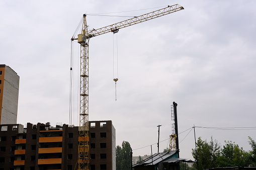 A crane builds a house at a height, lifts the load to the upper floor. The construction site of a residential building, a building against the sky. High quality photo.