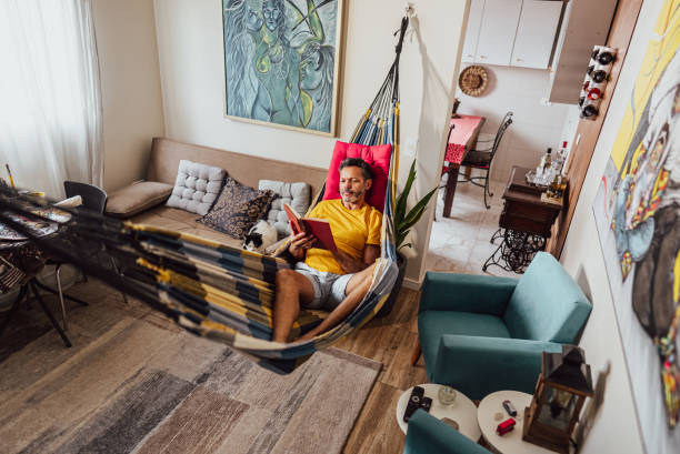 Mature man reading a book lying down on hammock at home