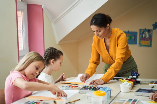 Beautiful woman helping children learn drawing in class room