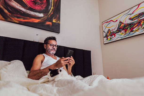 istock Mature man using mobile phone on bed in the bedroom at home 2150338404