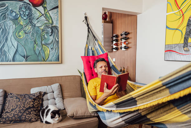 istock Mature man reading a book lying down on hammock at home 2150338467