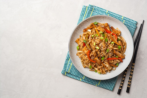 Stir fried udon noodles with chicken and vegetables in plate on concrete background. Top view, copy space.