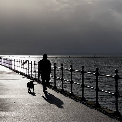 Silhouette of a man walking a dog at marine lake, West Kirby