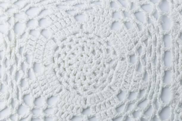 A white crocheted piece of fabric with a pattern of a flower. The flower is made up of many small circles