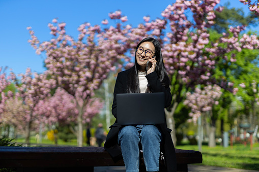 In the park, a smart and tech-savvy Japanese or Korean woman studies online with her laptop.