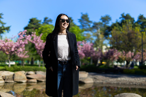 A stylish Japanese or Korean woman walks gracefully in the spring outdoors, exuding beauty and glamour.