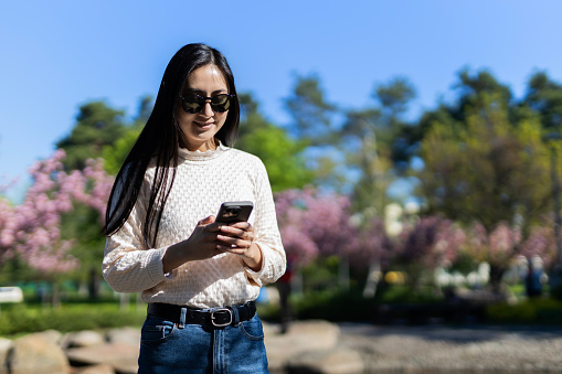 Japanese woman texts on her smartphone in the park, embracing modern communication outdoors.