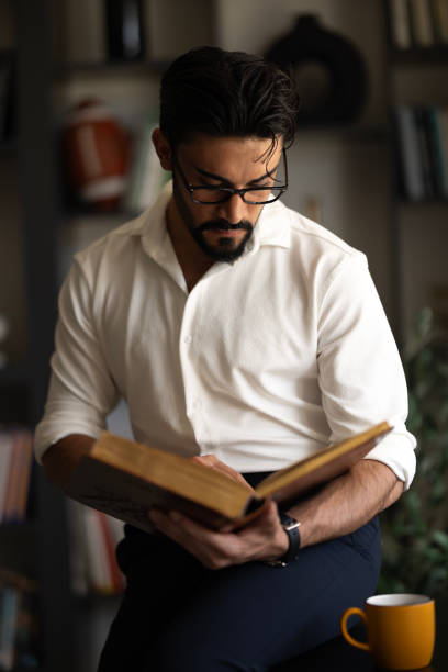 istock Young man reading book in the library 2150344417